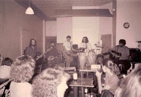 Cultural Attraction playing at Kilgore's circa late summer 1994. Says Mike Tulis, "The photograph is taken from the middle of the room; the stage is now where the Shelterbelt audience sits, and the Shelterbelt stage blocks the old entranceway to Kilgore's. The bar is off to screen right." From left on stage are Mike Tulis, Bob Garfield, Kevin McClay, John Riley and Milan Seth.